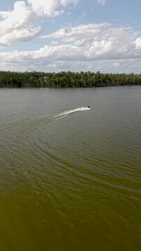 Stunning aerial view following a person riding a jet ski across the calm waters of Lake Dyer in Queensland, Australia, on a beautiful sunny day with a lush forest on the horizon
