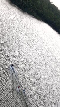 Aerial drone shot capturing a motorboat towing two people on inflatable tubes across the rippled water of Lake Dyer in Australia, creating a wake behind them on a sunny summer day