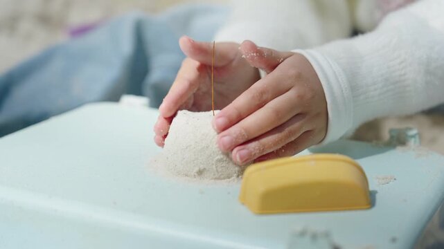 Toddler Hands Molding Cylindrical Shape in Playground with Yellow Toys