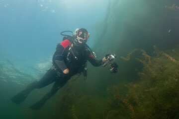 Older diver explore underwater site and capture moments using cameras during a diving session in clear water