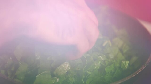 The process of washing and stewing spinach: wash men's hands under water, cut into pieces, throw in a frying pan, stir, prepare for freezing, make spinach pie