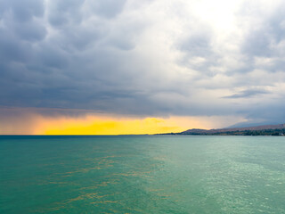 Fototapeta premium Sunset at Issyk Kul Lake in Kyrgyzstan. Bright sun breaking through clouds reflecting in clear turquoise water.