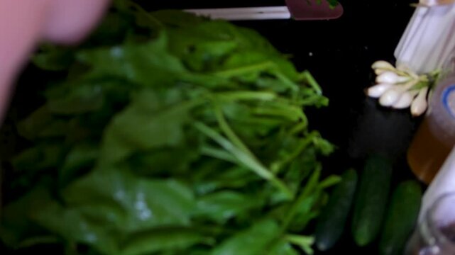 The process of washing and stewing spinach: wash men's hands under water, cut into pieces, throw in a frying pan, stir, prepare for freezing, make spinach pie