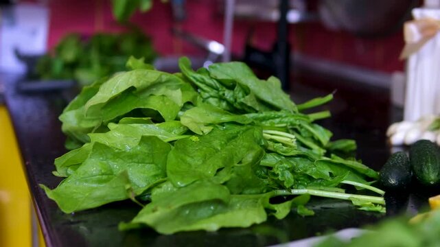 The process of washing and stewing spinach: wash men's hands under water, cut into pieces, throw in a frying pan, stir, prepare for freezing, make spinach pie
