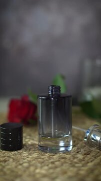 Vertical video of dropping essential oils into black perfume bottle. Natural homemade fragrance creation with luxury aesthetic and red rose background.