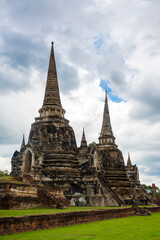 Fototapeta premium The three iconic restored chedis (stupas) at Wat Phra Si Sanphet in Ayutthaya, Thailand. The massive, bell-shaped structures stand in a row on a raised platform covered in green grass. Cloudy day.