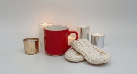 Fototapeta premium Seasonal red mug paired with mittens and glowing candles on copy space background