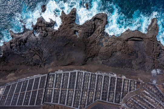 Aerial view of volcanic rock formations meet the turbulent ocean waves near salt pans, creating a striking contrast of textures and colors, Santa Cruz de La Palma, Canarias, Spain.