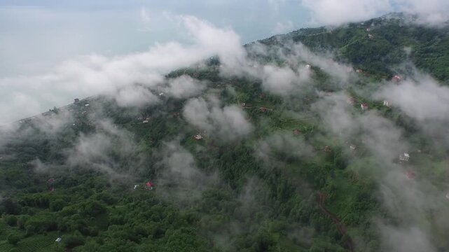 Aerial view of village houses in scattered settlements in clouds over rainforest in Black Sea Turkey geography. Mist drifts above green hills, revealing remote villages and lush mountain scenery.