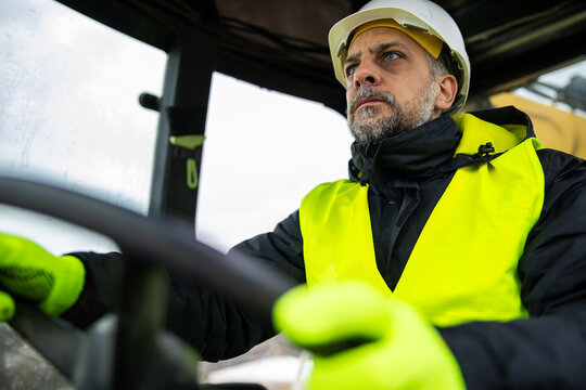 Construction worker operating backhoe loader inside cabin