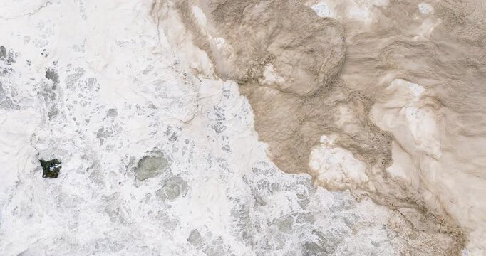 Sea foam and dirty ocean scum with dark brown and black sediment from storm surge in Nazare, Portugal. Climate change and higher rising sea levels