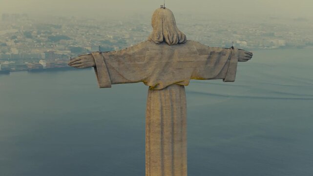 Drone view of the Christ the King monument in Almada, Portugal, with the 25 de Abril Bridge spanning the Tagus River and Lisbon visible in the background.
