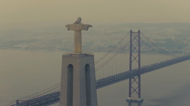 Drone view of the Christ the King monument in Almada, Portugal, with the 25 de Abril Bridge spanning the Tagus River and Lisbon visible in the background.
