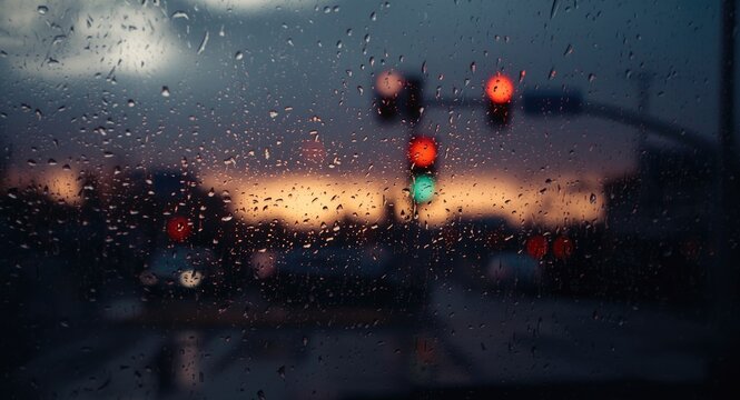 Urban traffic lights seen through rain splattered window pane at dusk