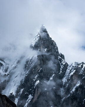 View of a majestic, snow-dusted mountain peak piercing through swirling clouds, a symphony of white and gray in the Peruvian Andes, Ancash, Peru.