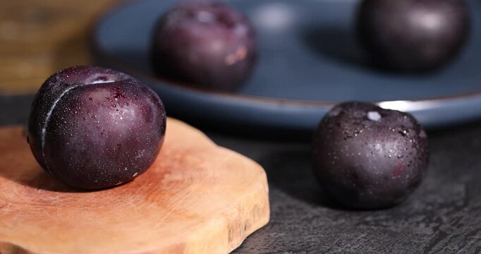 black fresh juicy wet plums on the kitchen table, several clean black plums on the table, the plums are covered with a lot of drops of water