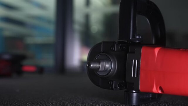 Detailed view of a red and black electric power tool on a carpeted floor, highlighting its construction and design.