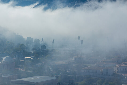 View of a city shrouded in a veil of mist, where buildings and structures emerge subtly against the backdrop of hazy mountains, Muzaffarabad, Azad Kashmir, Pakistan.