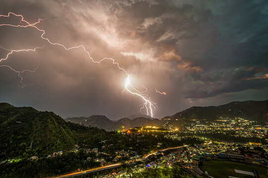 View of lightning strikes illuminating the sky above the mountainous landscape and the city lights below, casting an ethereal glow, Muzaffarabad, Azad Kashmir, Pakistan.