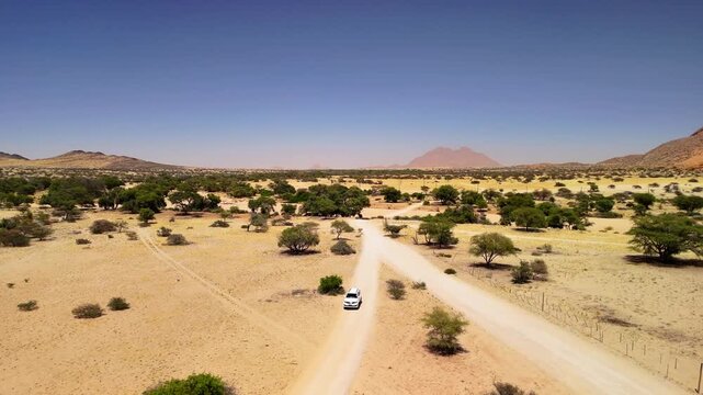 Drone Footage of White SUV Driving on African Riverbed and Sand Road with Mountain Landscape &ndash; Namibia 4K