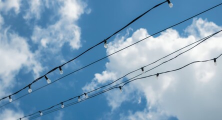 Small delicate lights positioned on narrow wires photographed from a low angle below a sharp blue sky and notable white clouds