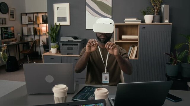 African American young male QA specialist with headset testing augmented reality application sitting at work table in office of tech company