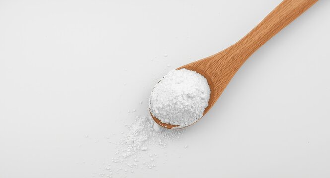 Overhead shot of wooden spoon containing bright sodium carbonate powder on clean backdrop