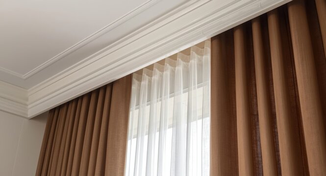 Close up of room interior showing white ceiling with plastic cornice rails and layered curtains including brown matt and see through fabric
