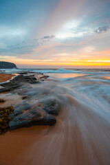 Naklejka premium Wave water flowing into the sandy and rocky beach shore.