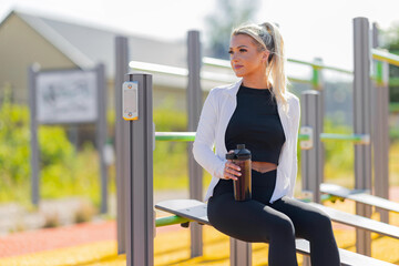 Woman resting after outdoor workout holding a shaker in a modern fitness park