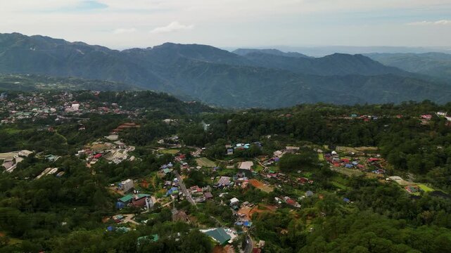 Panoramic overhead drone shot of quaint village town amid lush greenery and mountainous background - La Trinidad, Benguet, Philippines