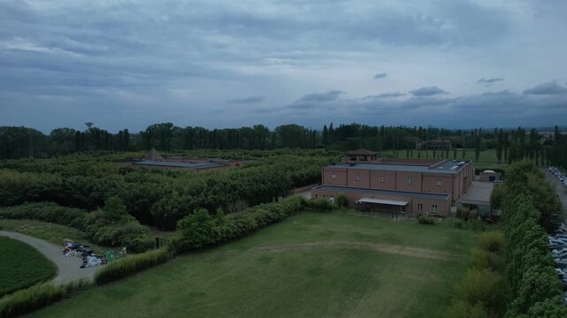 Labirinto della Masone bamboo maze in Fontanellato, Parma province, Italy, showing the geometric labyrinth, museum buildings, green hedges and flat Po Valley landscape under cloudy sky, drone descent