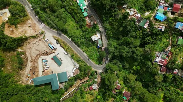 Aerial top-down view of winding mountain road amid lush forest greenery and house rooftops at La Trinidad, Benguet, Philippines