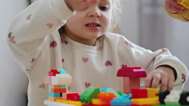 Two children are focused on building with colorful blocks on a table in a bright room while enjoying their time together
