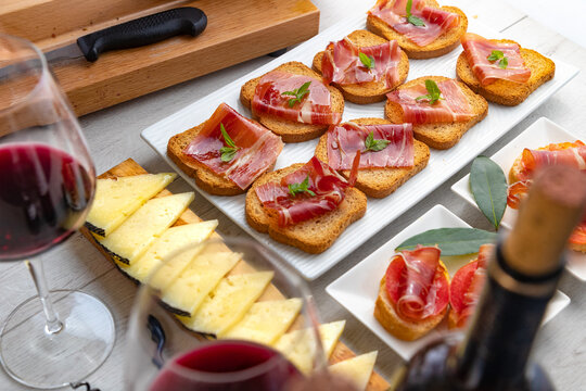 Tapas espa&ntilde;olas con jam&oacute;n, queso y vino tinto.Variedad de tapas espa&ntilde;olas con pan tostado, jam&oacute;n curado, lonchas de queso y copas de vino tinto sobre mesa r&uacute;stica. Presentaci&oacute;n elegante y concepto 