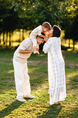 Fototapeta premium Happy Young Family Playing Outdoors While Father Gives Son A Shoulder Ride And Mother Kisses Him
