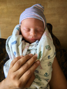 Overhead view of a newborn baby boy wrapped in a blanket on a man's lap