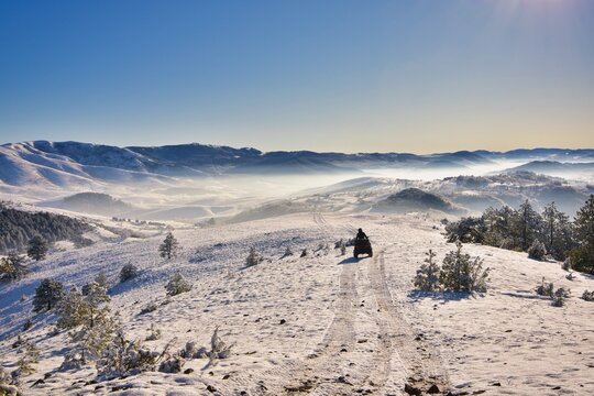 Rear view of a man driving a quadbike off road through a snowy mountain landscape, Mt Zlatibor, Serbia