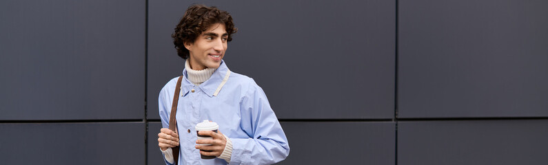 Handsome young man with curly hair enjoys coffee on a city street