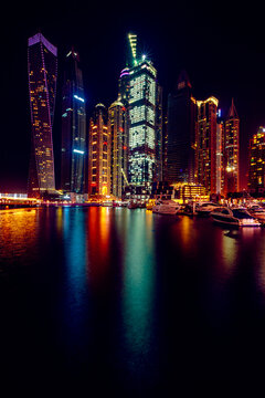 View into land of illuminated skyscrapers and yachts moored in Dubai marina at night, Dubai, UAE