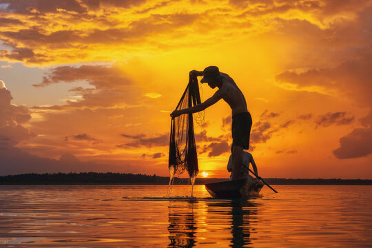 Silhouette of two fisherman in a fishing boat casting a fishing net at sunrise, Thailand