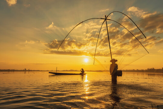 Silhouette of two fisherman in a fishing boat casting a fishing net at sunrise, Thailand