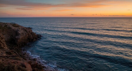Fototapeta premium Warm sunset hues highlighting craggy shoreline and rhythmic waves in a picturesque seashore
