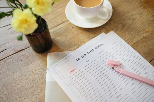 Overhead view of a highlighter pen on a to do list with a cappuccino and bunch of flowers in a vase on a wooden table