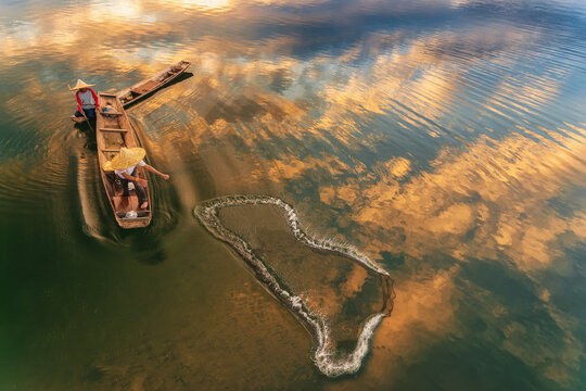 Overhead view of two fisherman in a fishing boat casting a fishing net at sunrise, Thailand