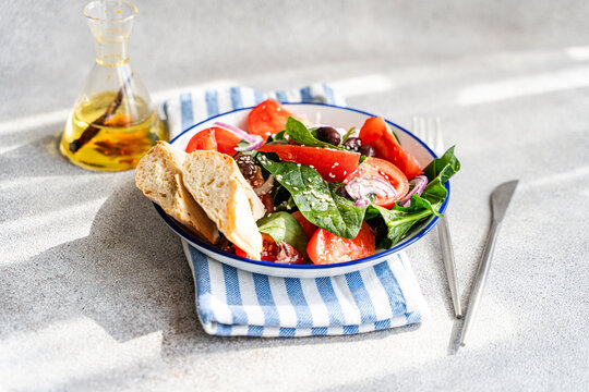 Close-up of a healthy plate of salad with spinach, tomatoes, red onion, olives, sesame seeds and bread on a folded napkin with a bottle of spicy chilli olive oil
