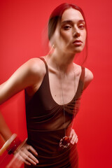 Fototapeta premium Stylish woman poses gracefully against a vibrant red backdrop showcasing modern fashion artistry
