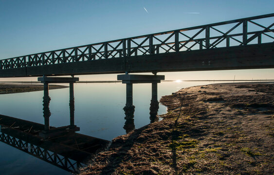 Ponte di legno attraversante la bassa marea dove si specchia, durante un soleggiato tramonto invernale 
