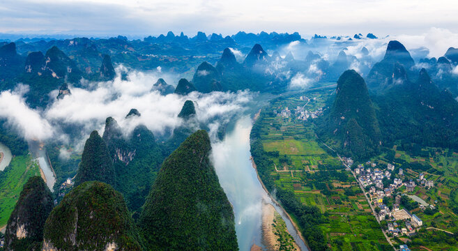 Breathtaking aerial view of the Li River winding through karst mountain peaks and rural villages under a sea of clouds in Guilin, China.