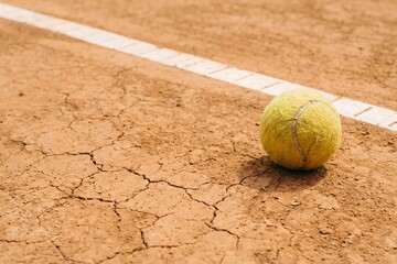Worn Tennis Ball on Dry Cracked Clay Court with White Line Depicting Abandonment of Sports